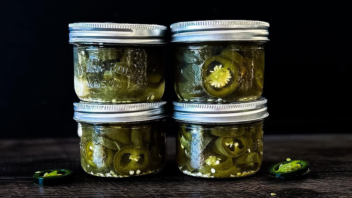 Four jars of homemade canned jalapeño peppers filled with sliced peppers and pickling brine.