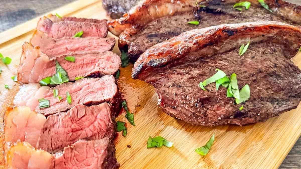 Smoked picanha steak sliced on a wooden cutting board, showing juicy medium-rare beef with a crispy fat cap and fresh herb garnish.