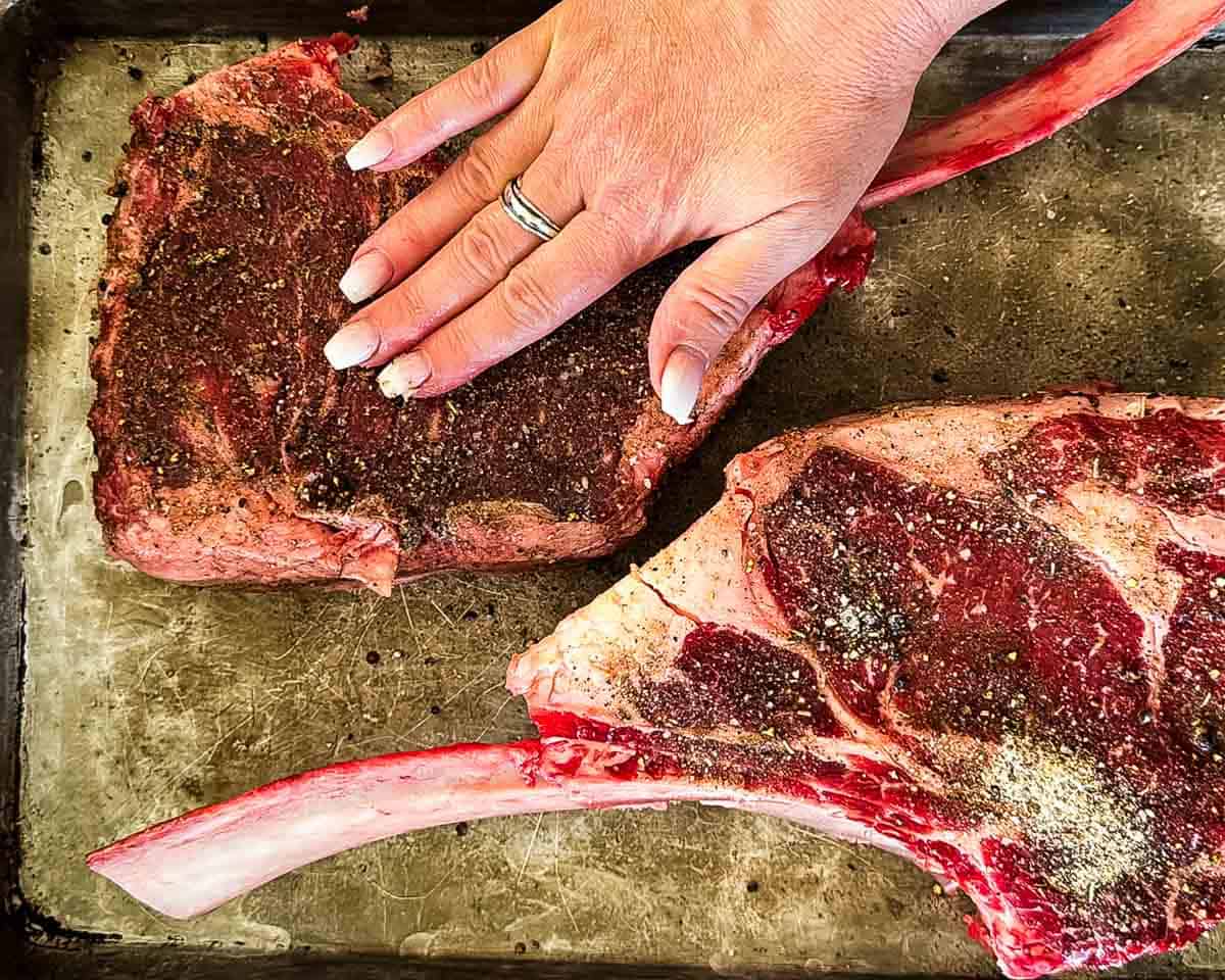 Seasoning tomahawk steaks with homemade steak rub before smoking.