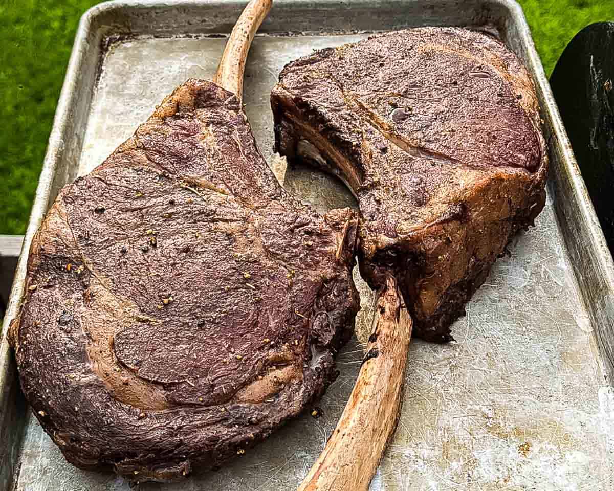 Smoked tomahawk steaks resting on a sheet pan before the reverse sear.