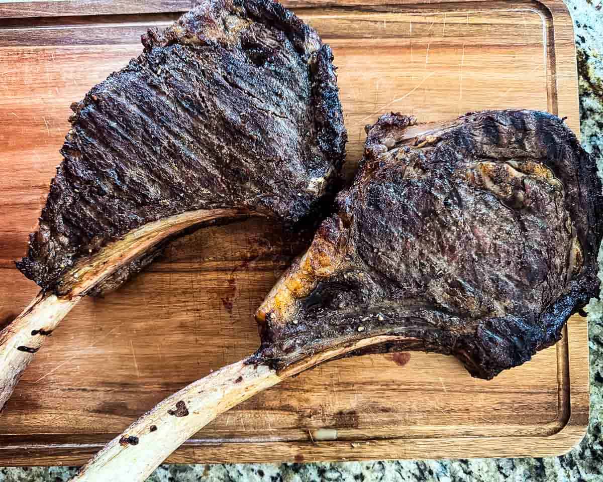 Smoked tomahawk steaks resting on a cutting board after reverse searing.