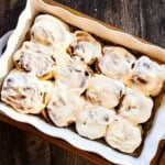 Soft sourdough discard cinnamon buns topped with vanilla icing in a baking dish.
