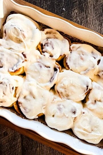 Soft sourdough discard cinnamon buns topped with vanilla icing in a baking dish.