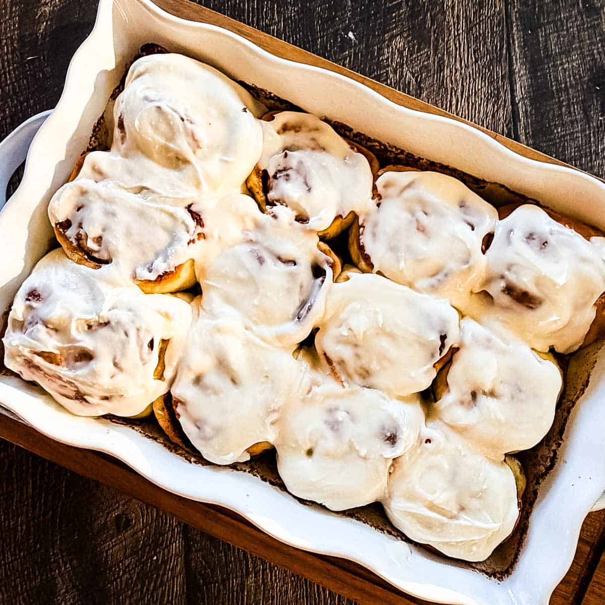 Soft sourdough discard cinnamon buns topped with vanilla icing in a baking dish.