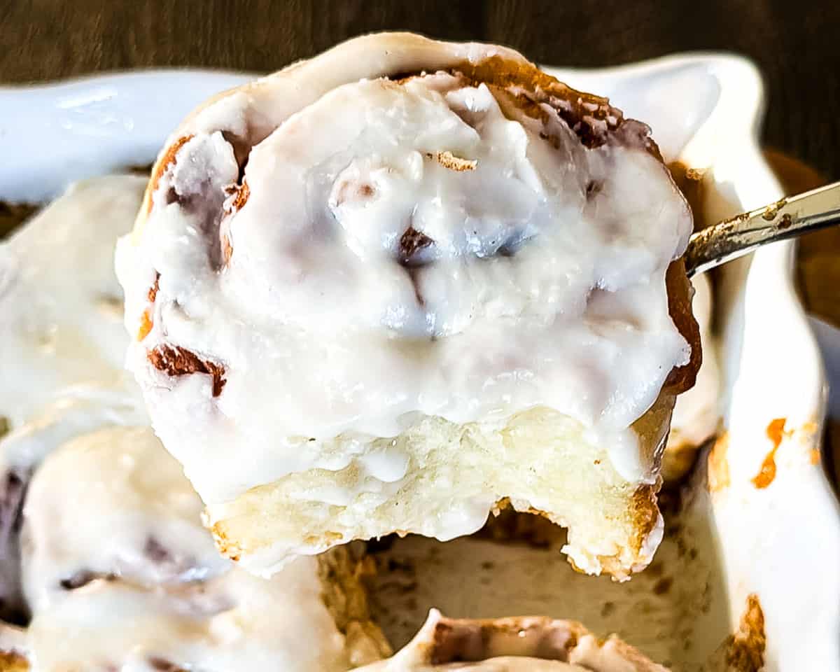 A fluffy cinnamon bun being lifted out of the baking dish.