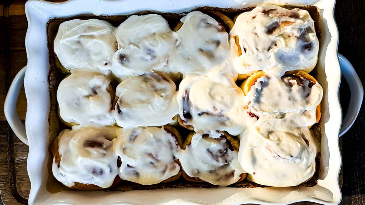 Soft and fluffy sourdough discard cinnamon buns topped with vanilla icing in a baking dish.