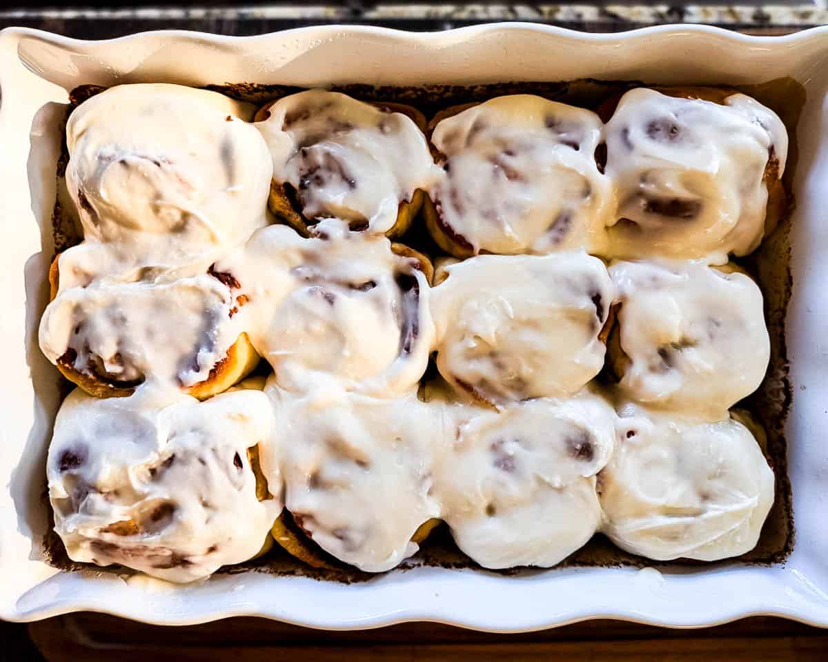 Freshly baked cinnamon buns covered with vanilla icing in a white baking dish.