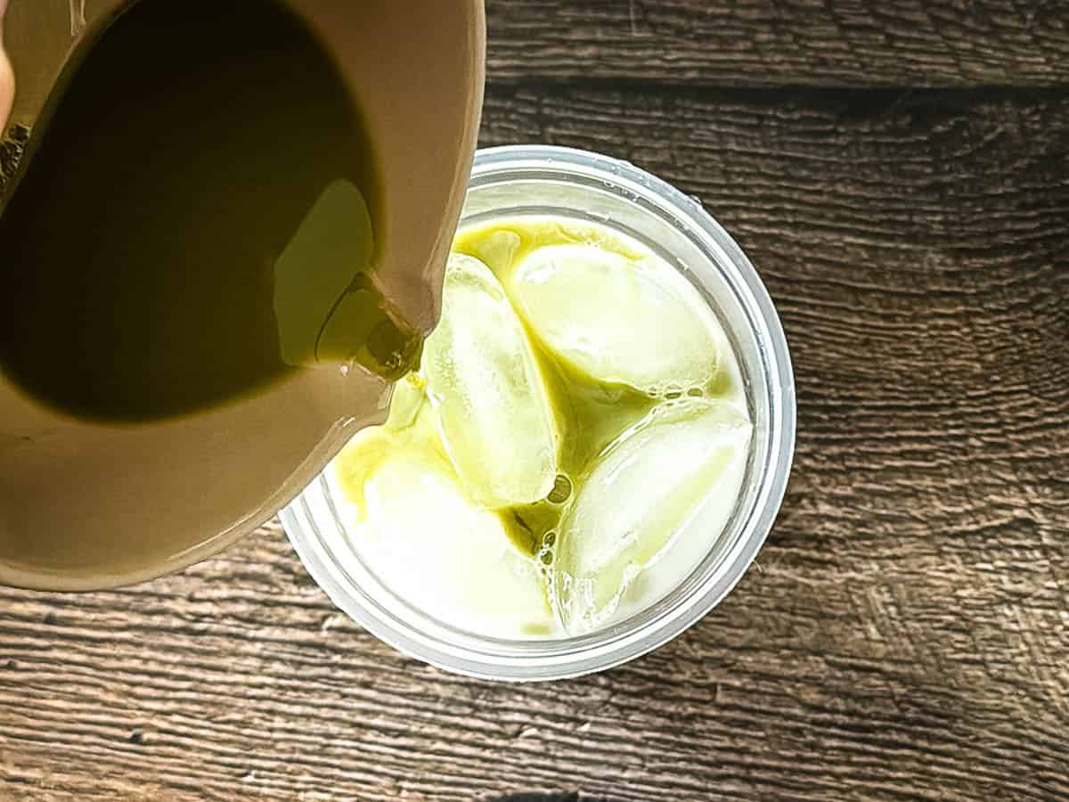Pouring whisked matcha over milk and ice for an iced matcha latte.