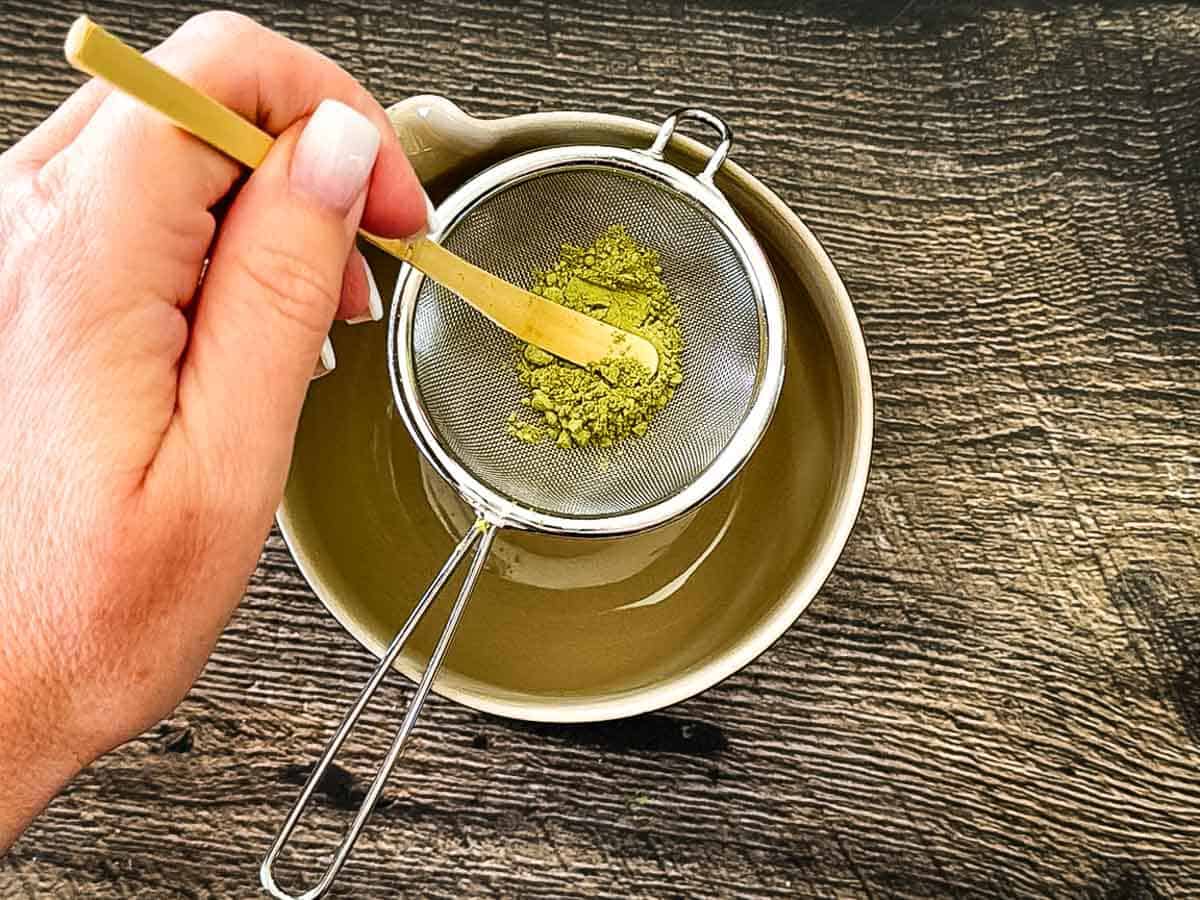 Sifting matcha powder through a fine mesh strainer to remove lumps.