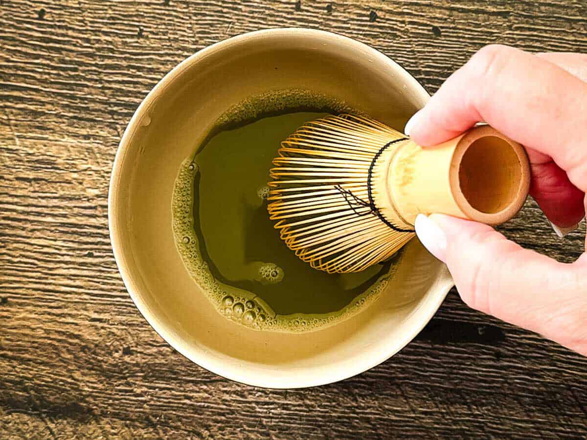 Whisking matcha and water with a bamboo matcha whisk until smooth and frothy.