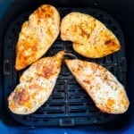 Four seasoned air fryer chicken breasts cooked until lightly golden in an air fryer basket.