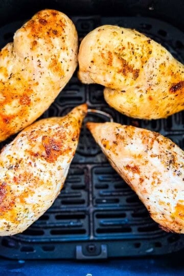 Four seasoned air fryer chicken breasts cooked until lightly golden in an air fryer basket.