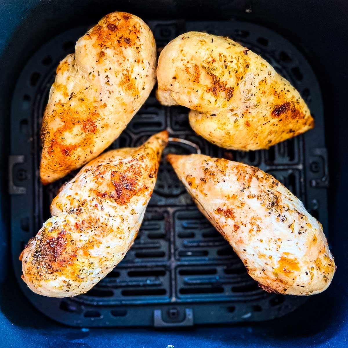 Four seasoned air fryer chicken breasts cooked until lightly golden in an air fryer basket.