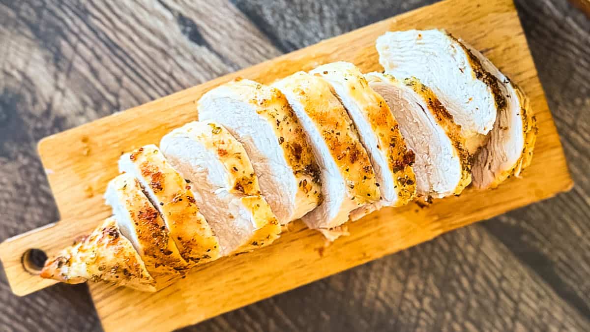 Sliced air fryer chicken breast seasoned with garlic and herbs on a wooden cutting board.