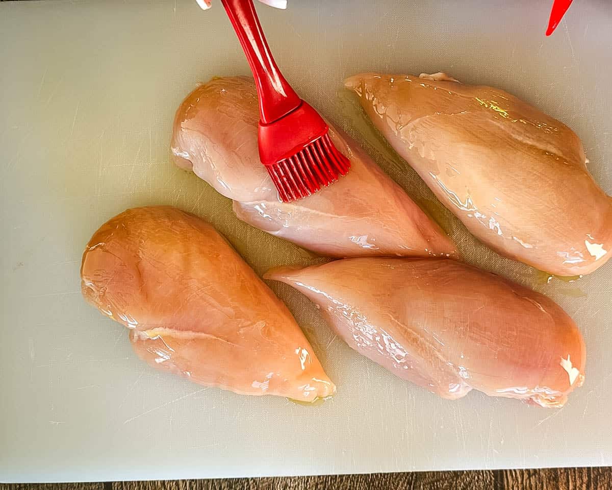 Brushing boneless skinless chicken breasts with olive oil before seasoning.