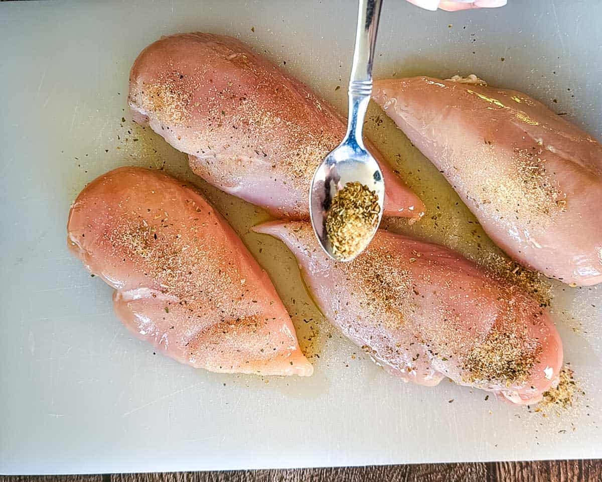 Sprinkling seasoning mixture over boneless skinless chicken breasts.