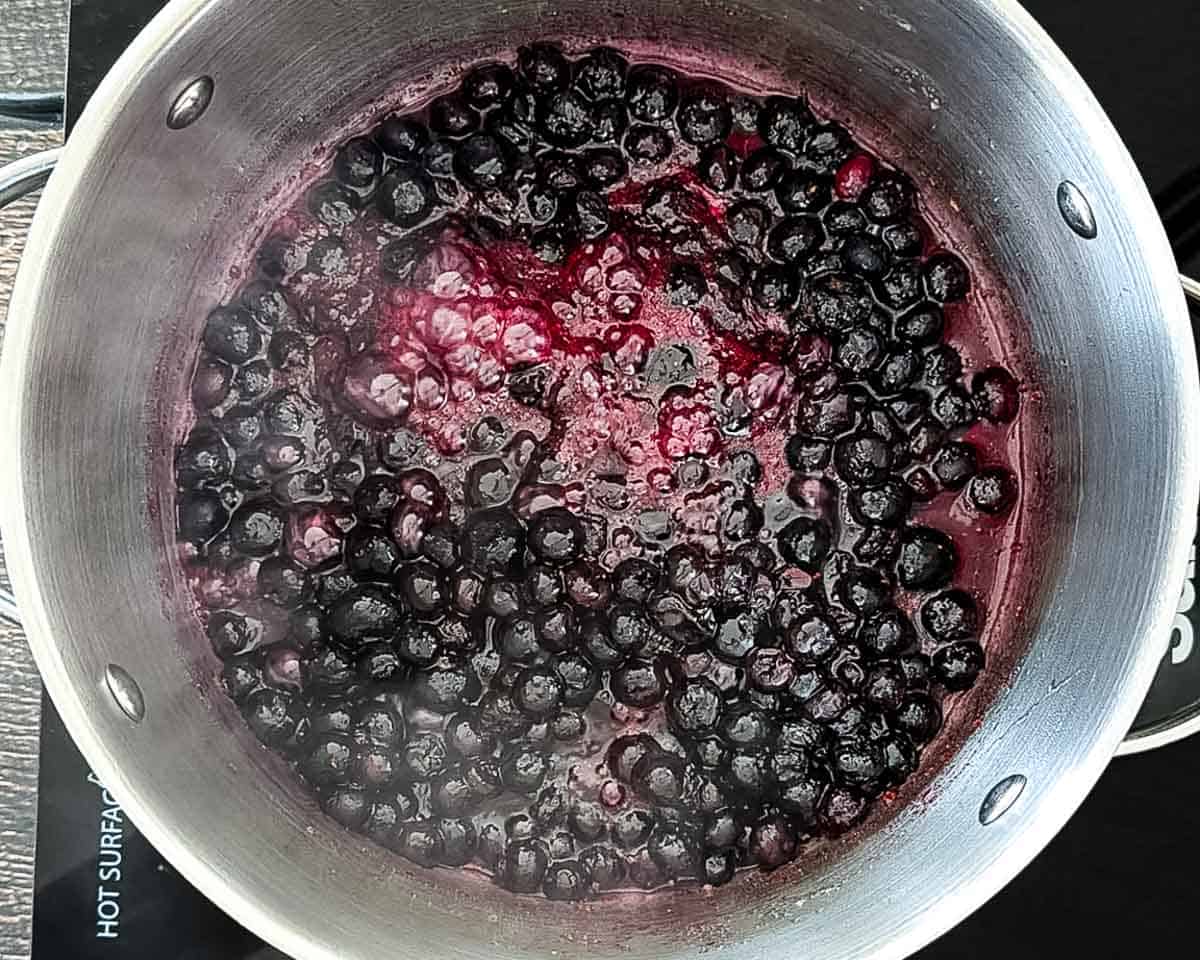 Blueberries cooking in a saucepan and beginning to release their juices.