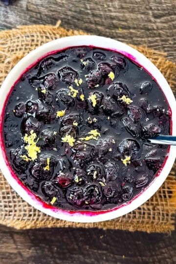 Homemade blueberry compote with whole blueberries and fresh lemon zest in a white bowl.
