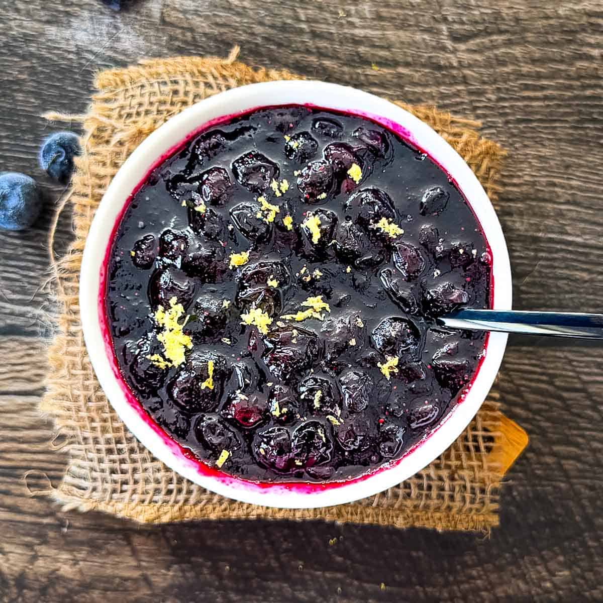 Homemade blueberry compote with whole blueberries and fresh lemon zest in a white bowl.