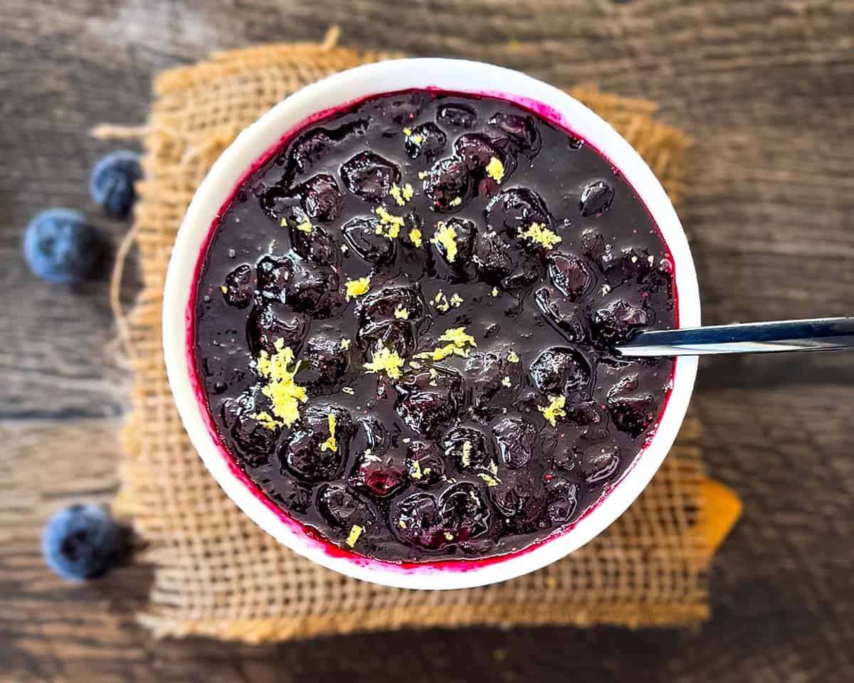 The finished blueberry compote ready to serve in a white bowl, garnished with lemon zest.