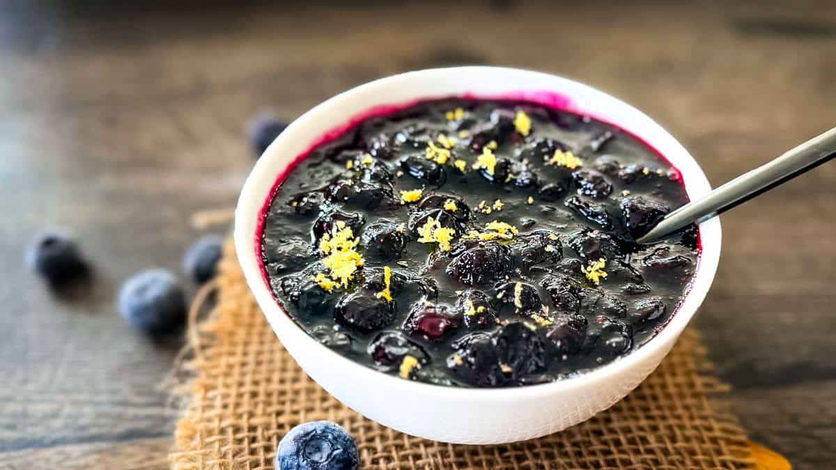 Homemade blueberry compote with whole blueberries and lemon zest in a white bowl.