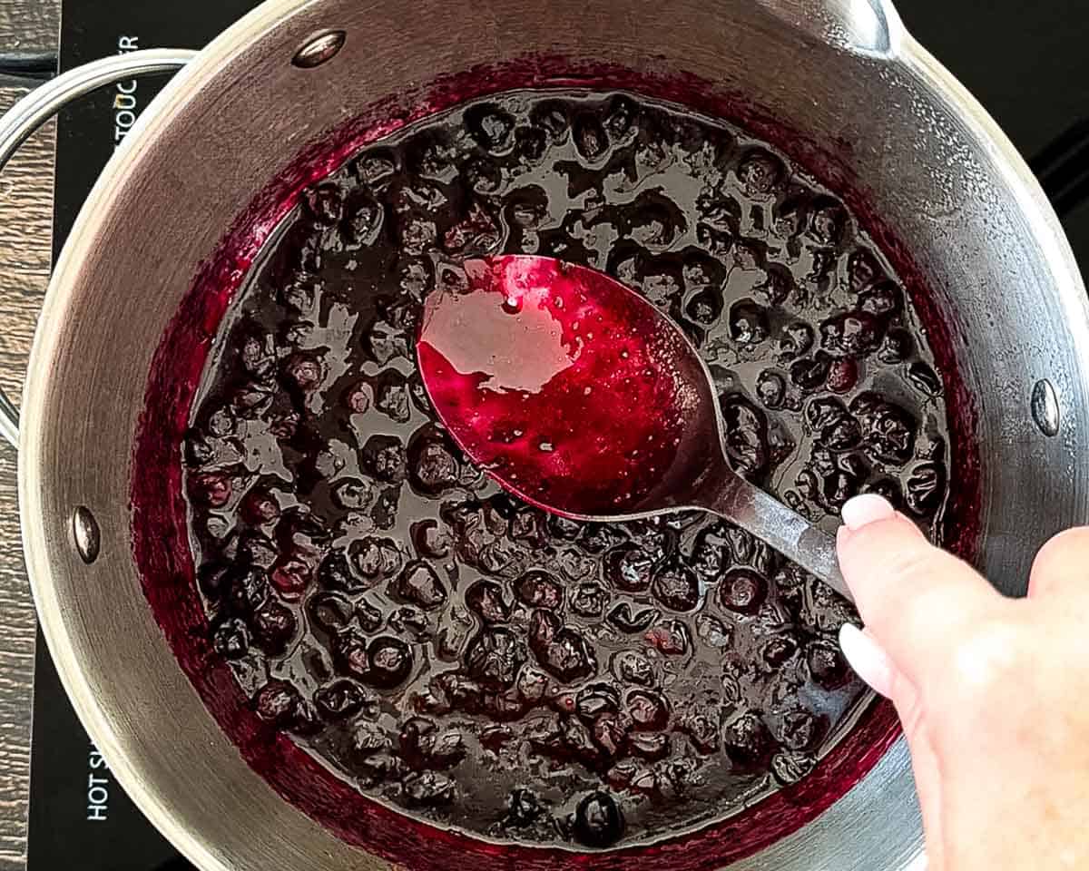 Gently mashing softened blueberries with a spoon while the blueberry compote simmers.
