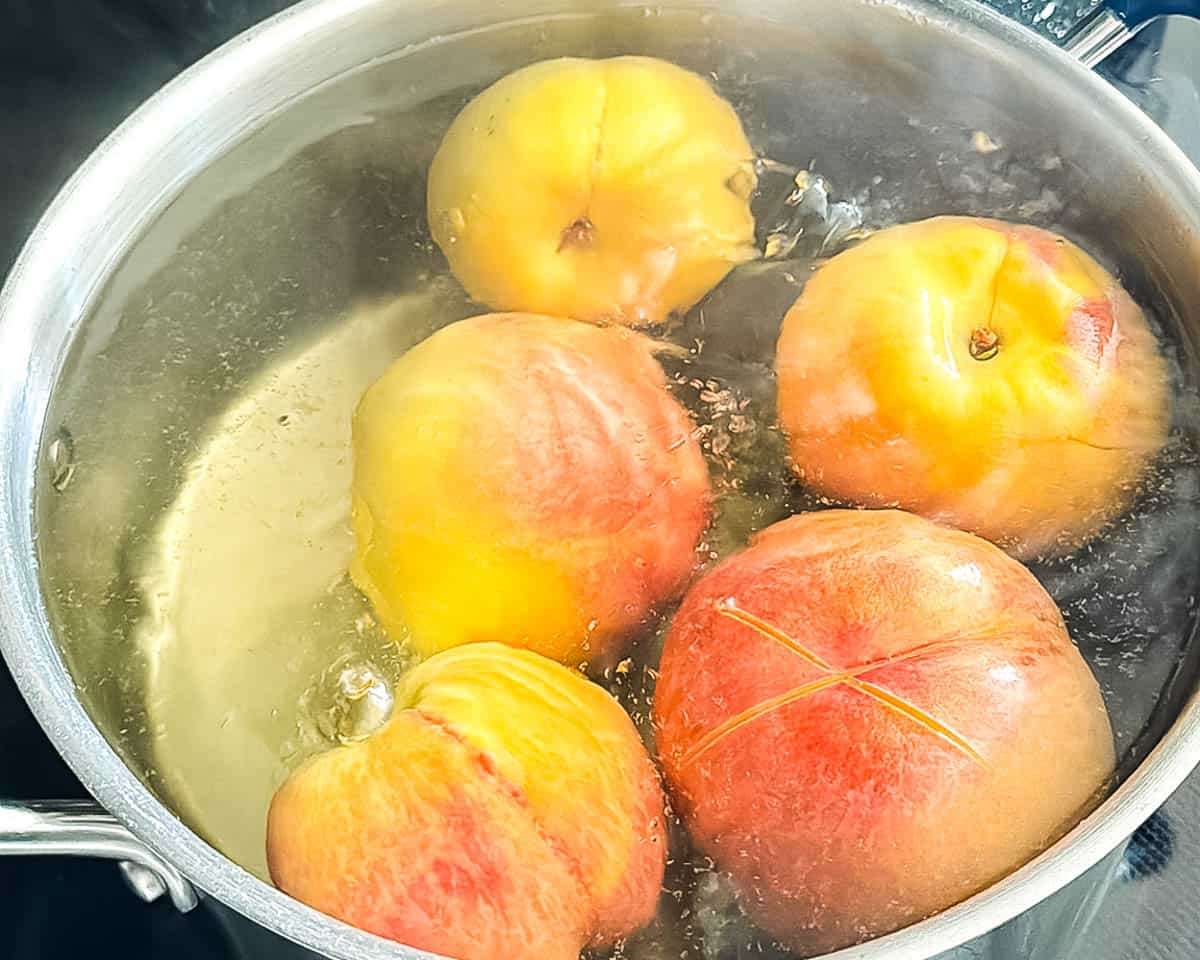 Yellow peaches blanching in boiling water to loosen the skins.