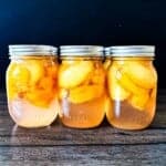 Pint jars of homemade canned peaches in syrup on a wooden table.