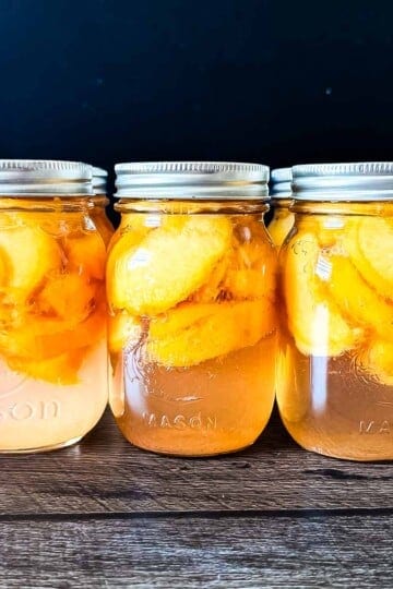 Pint jars of homemade canned peaches in syrup on a wooden table.
