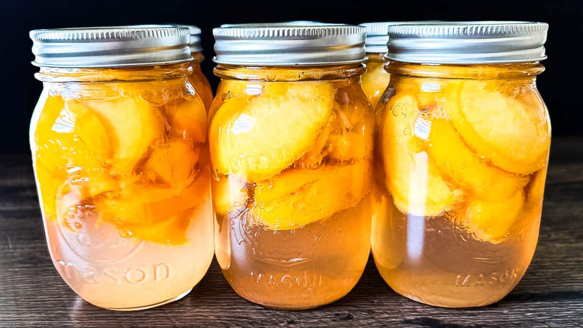 Cooled jars of canned peaches in pint jars with light syrup ready for storage.