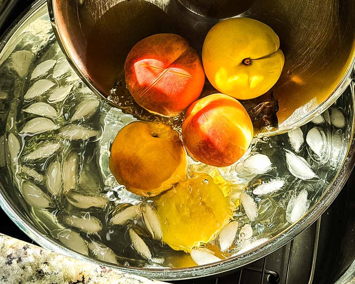 Blanched peaches being transferred to a bowl of ice water.