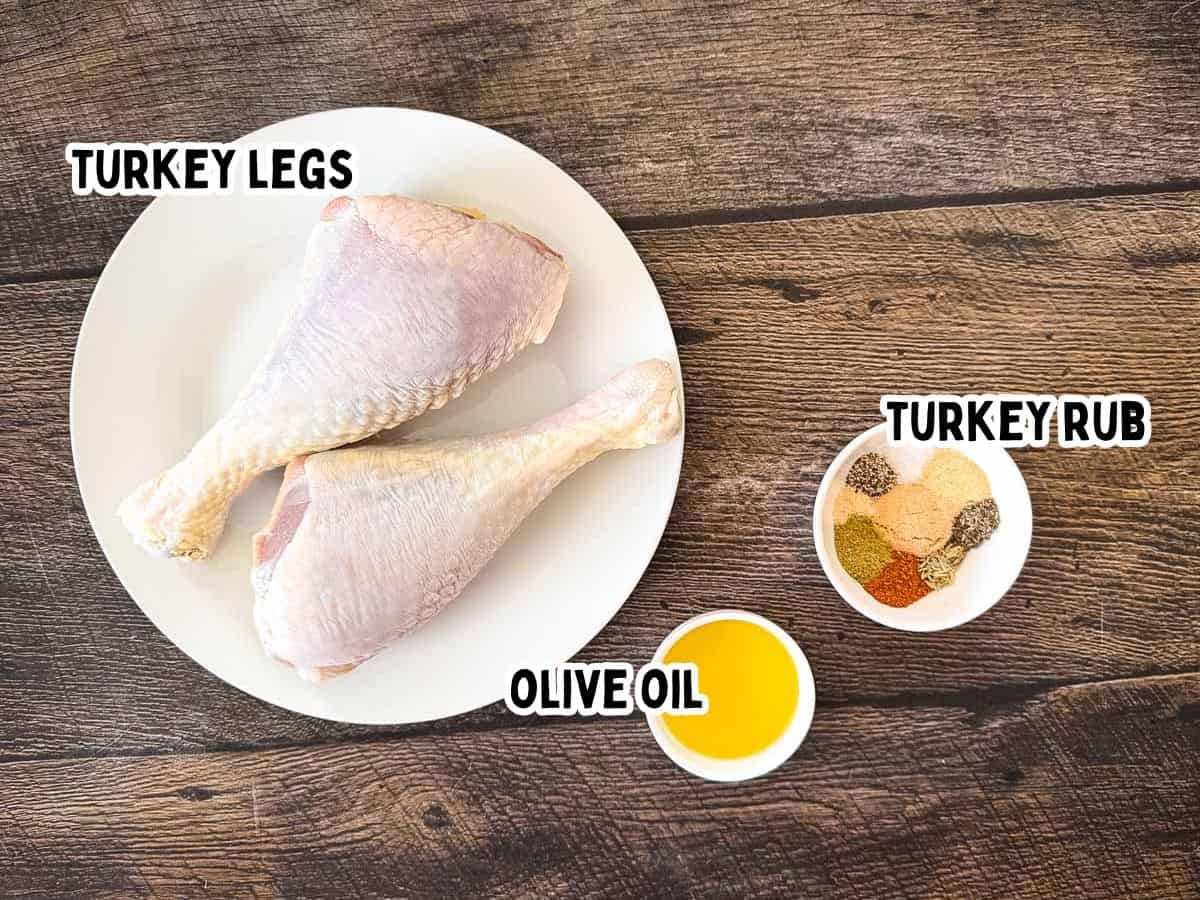 Raw turkey legs, olive oil, and homemade turkey rub arranged on a wooden table for smoked turkey legs.