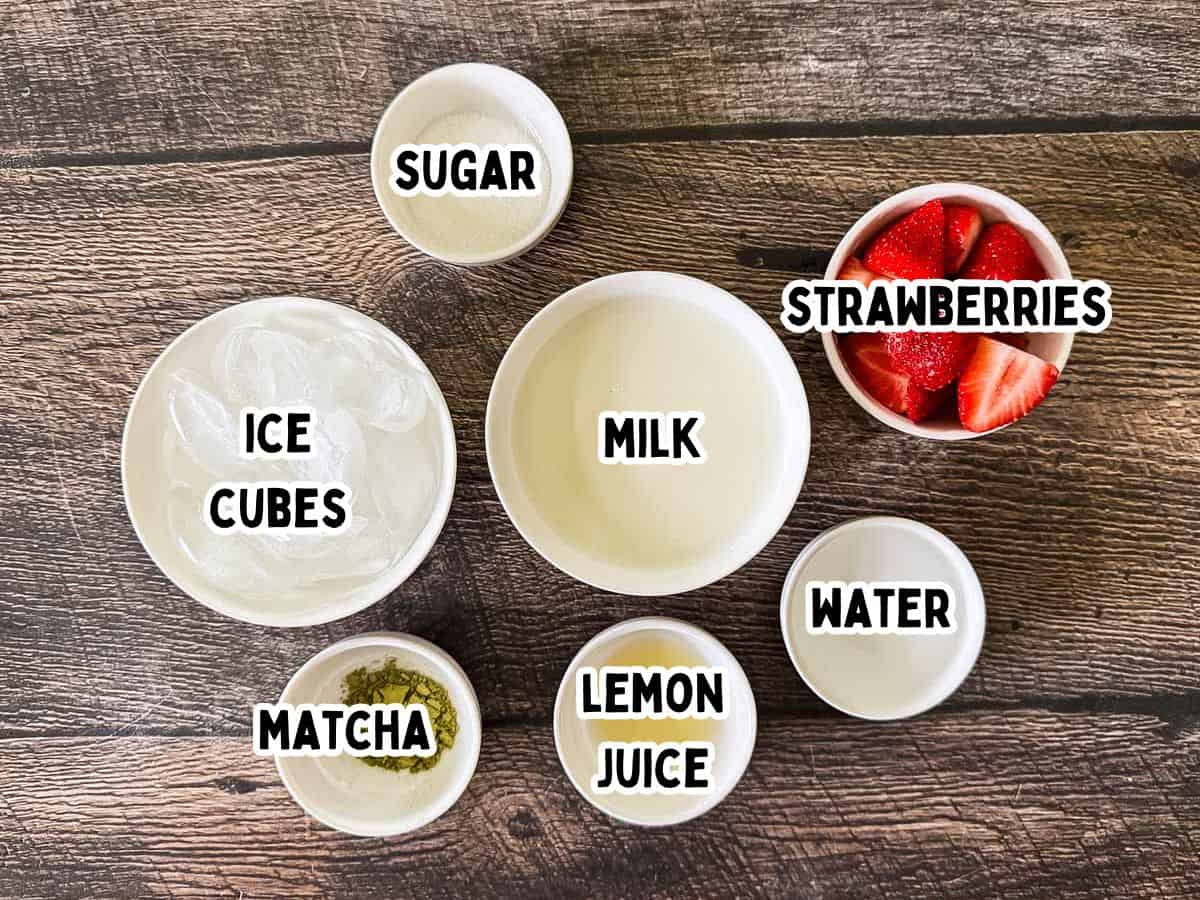 Labeled ingredients for strawberry matcha latte in small bowls on a wooden table.
