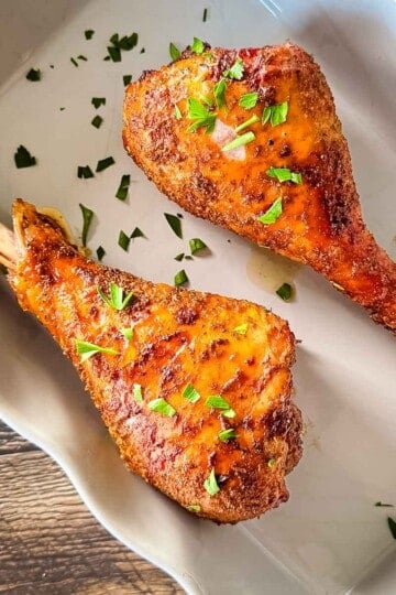 Smoked turkey legs smoked on a pellet grill with browned, seasoned skin and fresh parsley.