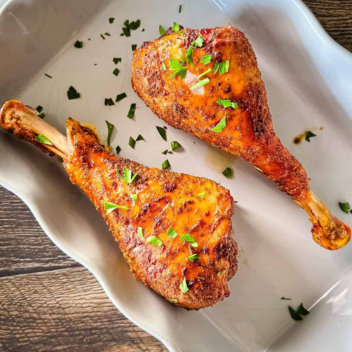 Smoked turkey legs smoked on a pellet grill with browned, seasoned skin and fresh parsley.