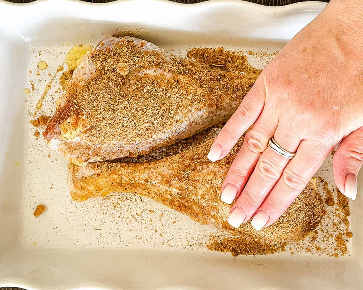 Pressing dry rub seasoning onto the turkey legs.