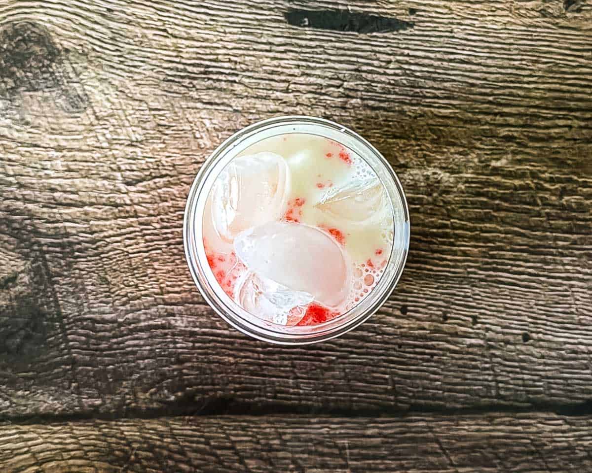 Strawberry puree, ice, and milk layered in a glass.