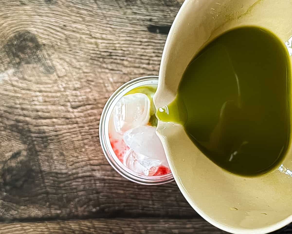 Prepared matcha being poured over milk and strawberry puree to make a strawberry matcha latte.