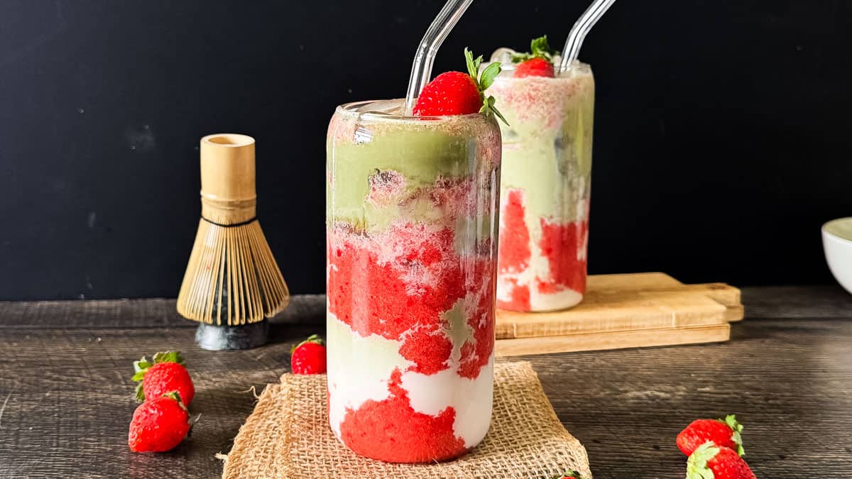 Two colorful strawberry and matcha smoothies with straws on a rustic table.