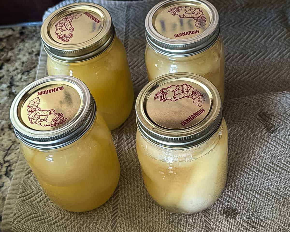 Processed jars of canned pears cooling on a towel after water-bath canning.