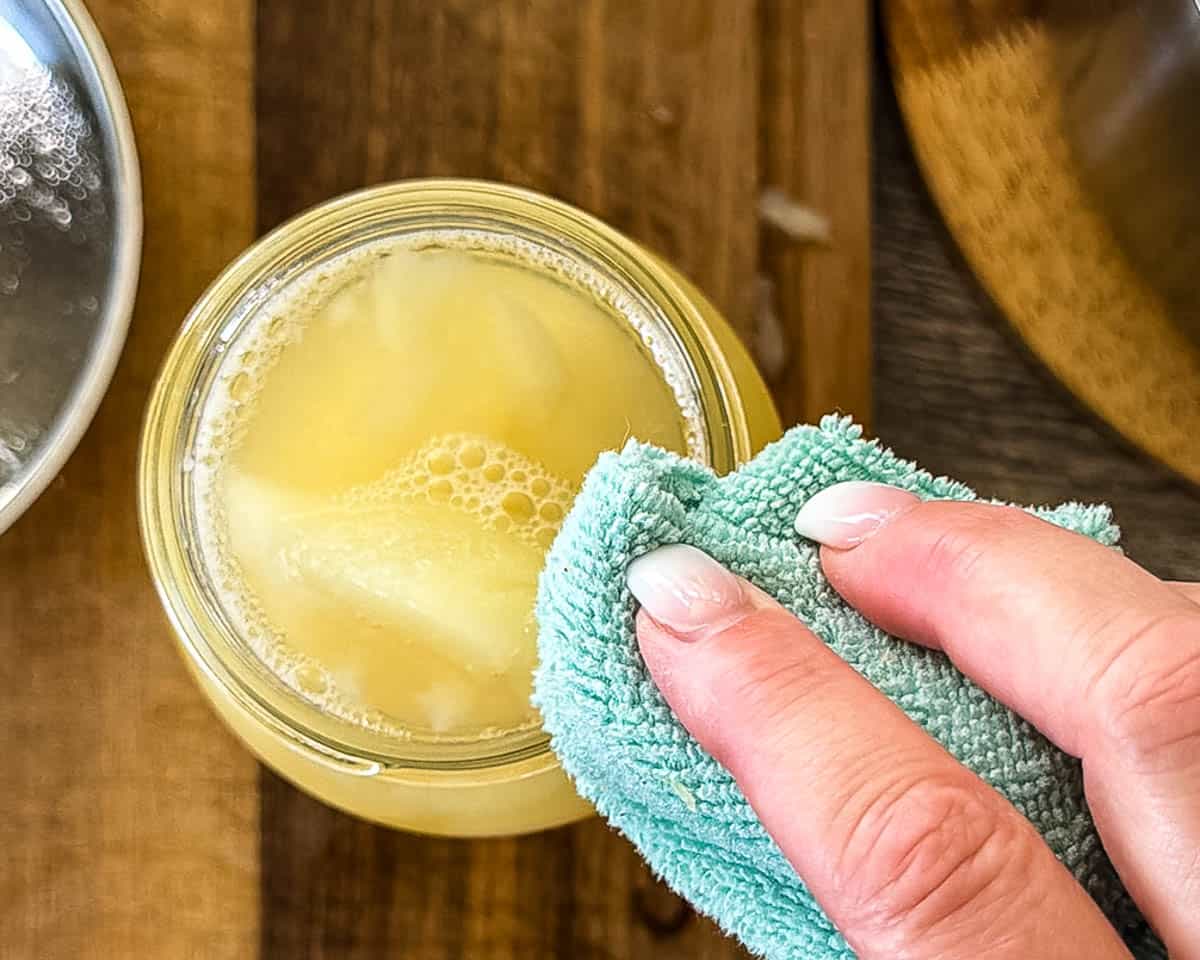 Wiping the rim of the canning jar filled with pears with a clean cloth.