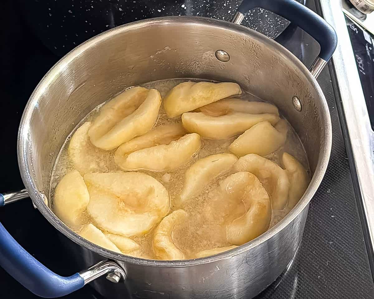 Pear halves simmering in light syrup for hot-pack canning.