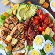 Grilled chicken avocado caesar salad on a white plate.