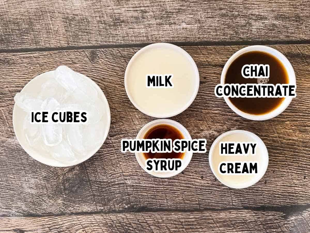 Labeled ingredients for a pumpkin cream chai latte in white bowls on a wooden table.
