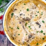 Cream of mushroom pork chops in a red cast iron skillet, bone-in chops covered in creamy mushroom gravy and fresh herbs.
