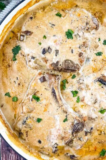 Cream of mushroom pork chops in a red cast iron skillet, bone-in chops covered in creamy mushroom gravy and fresh herbs.
