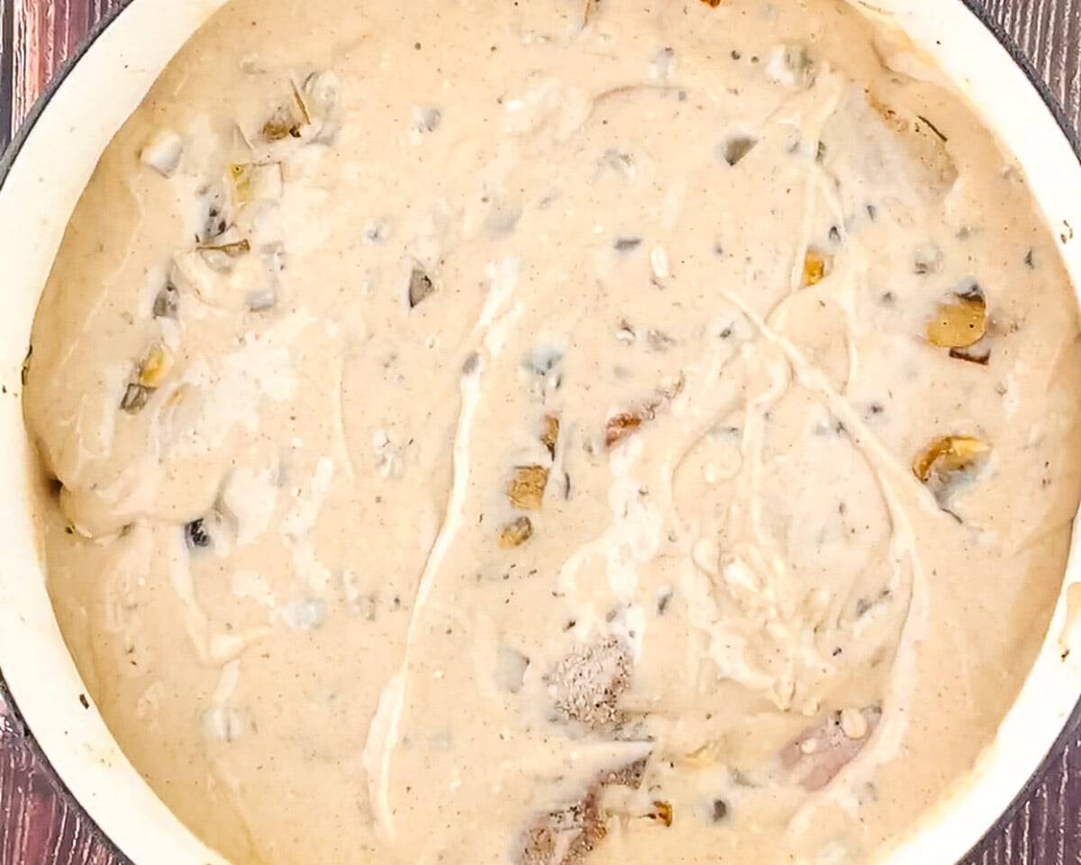 Cast iron skillet of bone-in pork chops fully covered in creamy cream of mushroom sauce before baking.