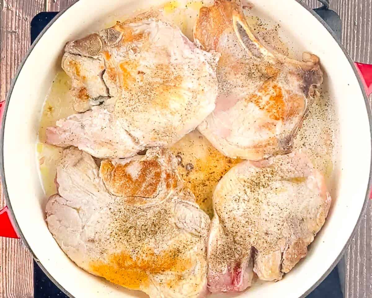 Four seared bone-in pork chops browned and seasoned with black pepper in a cast iron skillet.