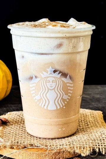 Iced pumpkin cream chai latte with pumpkin cold foam and a sprinkle of pumpkin pie spice in a reused Starbucks glass.