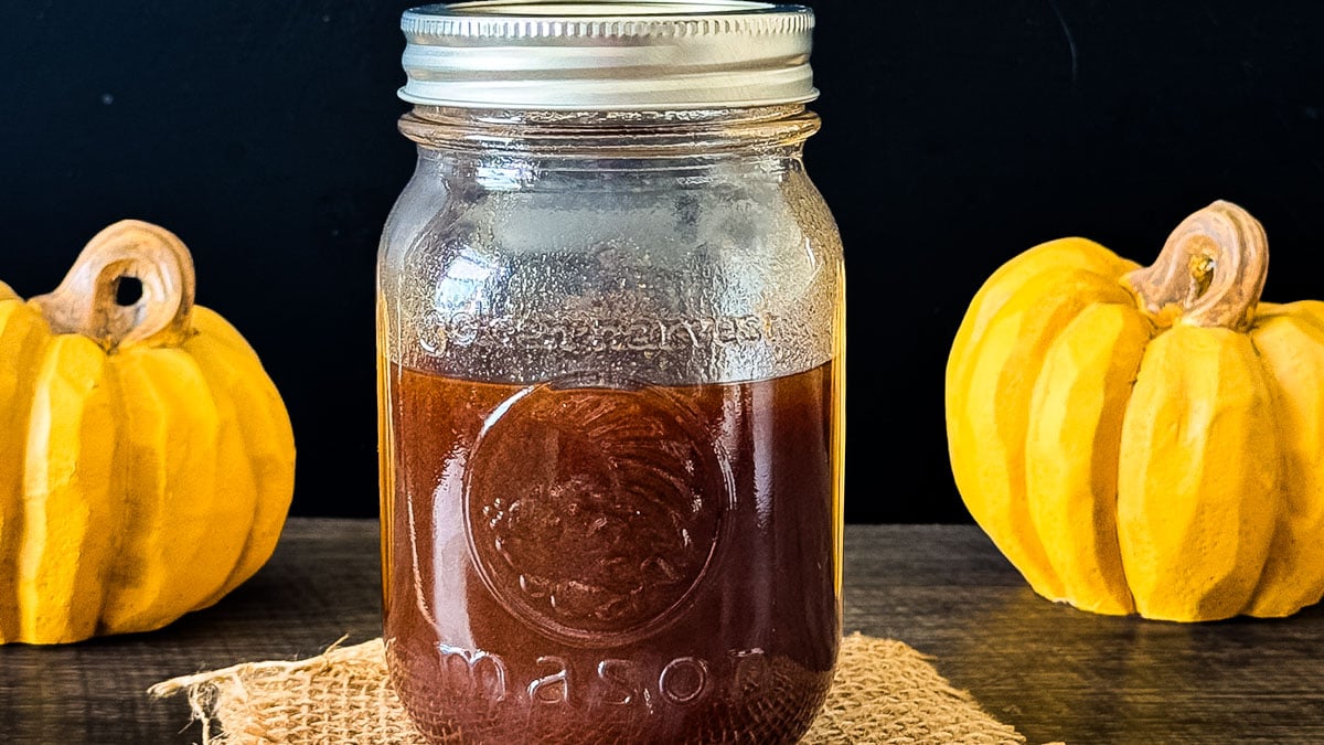 A glass jar filled with homemade pumpkin coffee syrup on a wooden table.